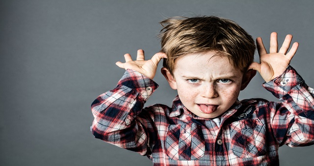 civility, incivility, angry little brat enjoying making a grimace, sticking out his tongue, playing with his hands for misbehavior, contrast effects, grey background