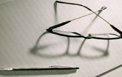 Glasses and pen on a piece of paper with shadows