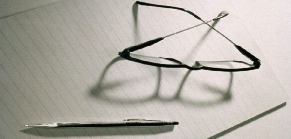 Glasses and pen on a piece of paper with shadows
