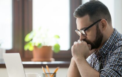 Person looking at computer while stressed and holding hands to chin