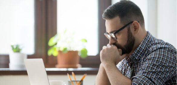 Person looking at computer while stressed and holding hands to chin