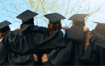 Group of students have graduation gowns and caps on and have their backs turned to camera while embracing