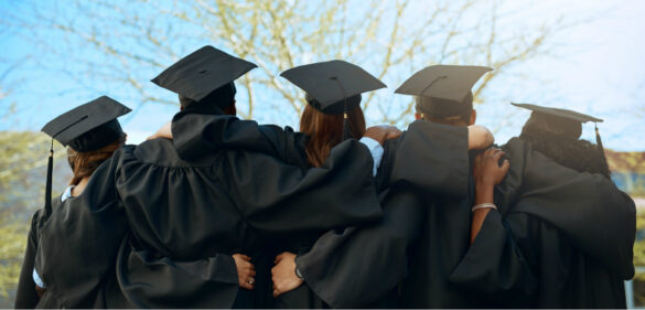 Group of students have graduation gowns and caps on and have their backs turned to camera while embracing