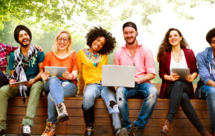 Group of diverse individuals sitting on bench with computers and smiling