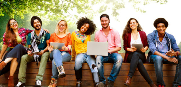 Group of diverse individuals sitting on bench with computers and smiling
