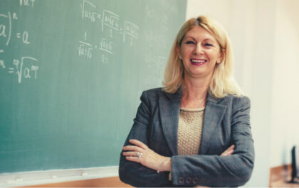 Woman standing in front of chalkboard with arms crossed and smiling
