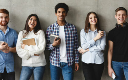 College students with books smiling to camera over grey wall, having break