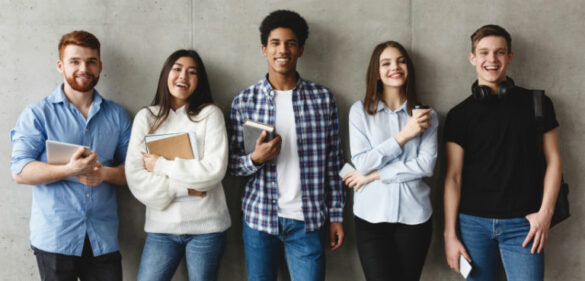 College students with books smiling to camera over grey wall, having break