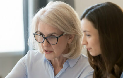 older woman in glasses-speaking-to-younger-woman-discussing-at-desk