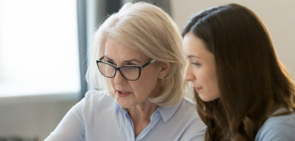 older woman in glasses-speaking-to-younger-woman-discussing-at-desk