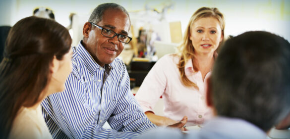 man-with-glasses-at-desk-with-other-colleagues-conversing