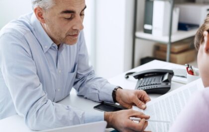 older-male-at-desk-showing-paper-to-female-colleague