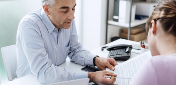 older-male-at-desk-showing-paper-to-female-colleague