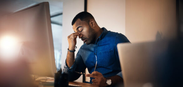man-at-desk-taking-his-glasses-off-hand-on-his-head-looking-tired