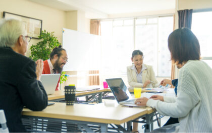 diverse-group-of-happy-people-working-in-a-room-smiling-at-a-desk-with-laptops