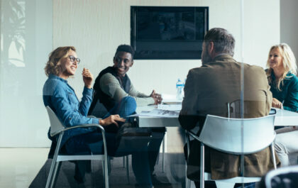 group-of-diverse-individuals-in-office-at-desk-happily-conversing-in-a-meeting