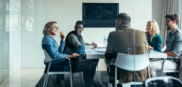 group-of-diverse-individuals-in-office-at-desk-happily-conversing-in-a-meeting