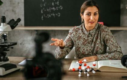 female-educator-at-desk-in-classroom-presenting-in-front-of-camera