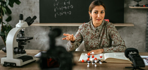 female-educator-at-desk-in-classroom-presenting-in-front-of-camera