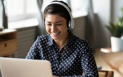 young-woman-with-headphones-at-desk-with-computer-happily-smiling