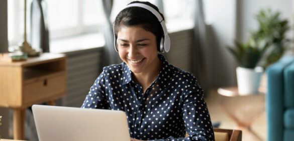 young-woman-with-headphones-at-desk-with-computer-happily-smiling
