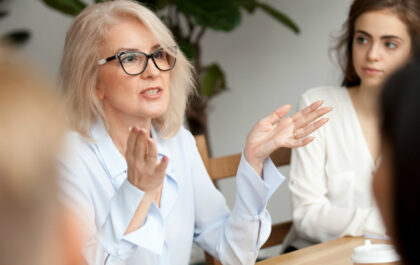 Businesswoman, teacher or mentor coach speaking to young people, senior woman in glasses teaching audience at training seminar, female business leader speaker talking at meeting (Attractive aged businesswoman, teacher or mentor coach s